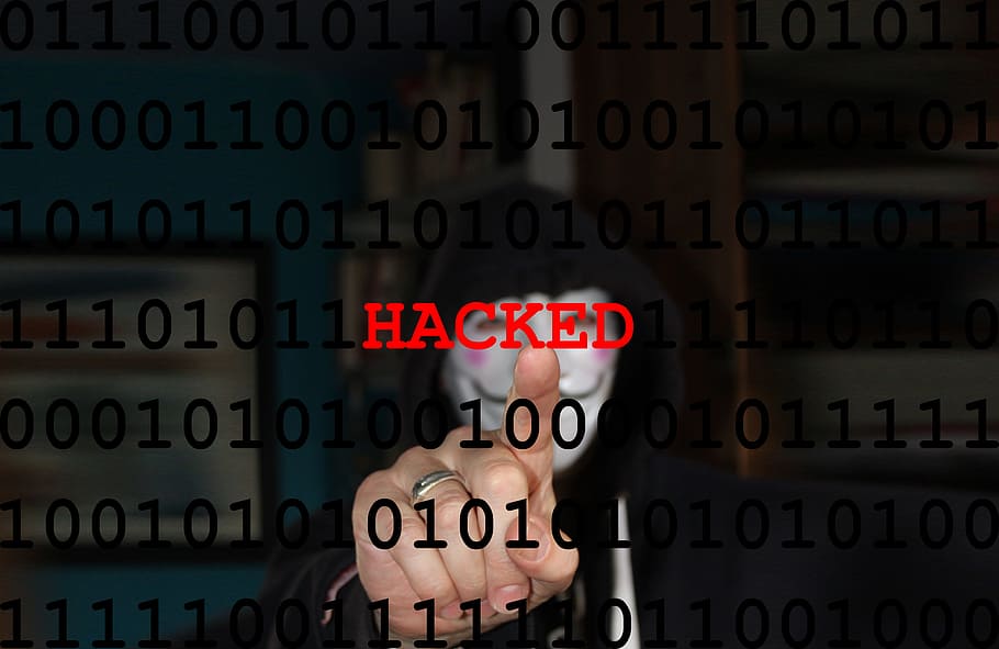 Seorang hacker dengan topeng menunjuk kata “password” di sebuah layar